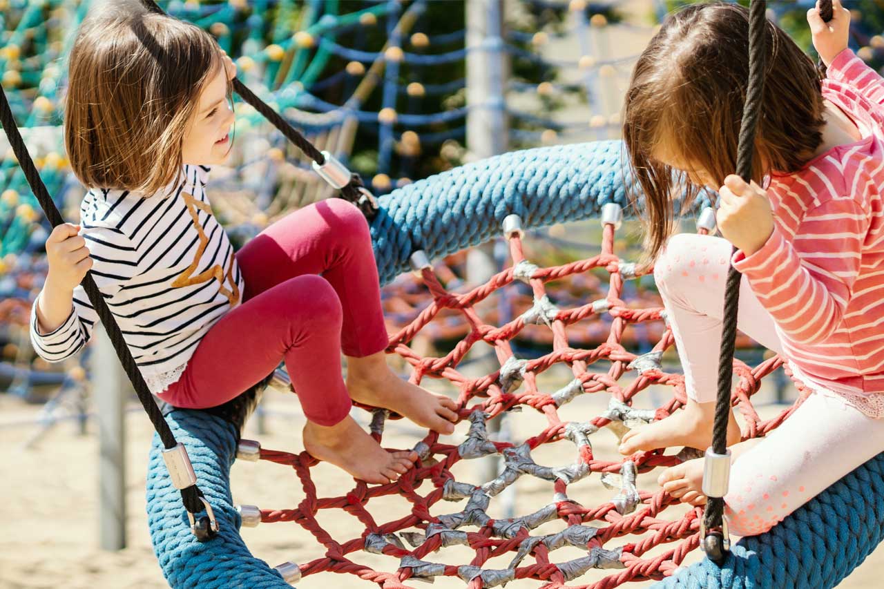 Zwei Mädchen sitzen auf einer Vogelnestschaukel.