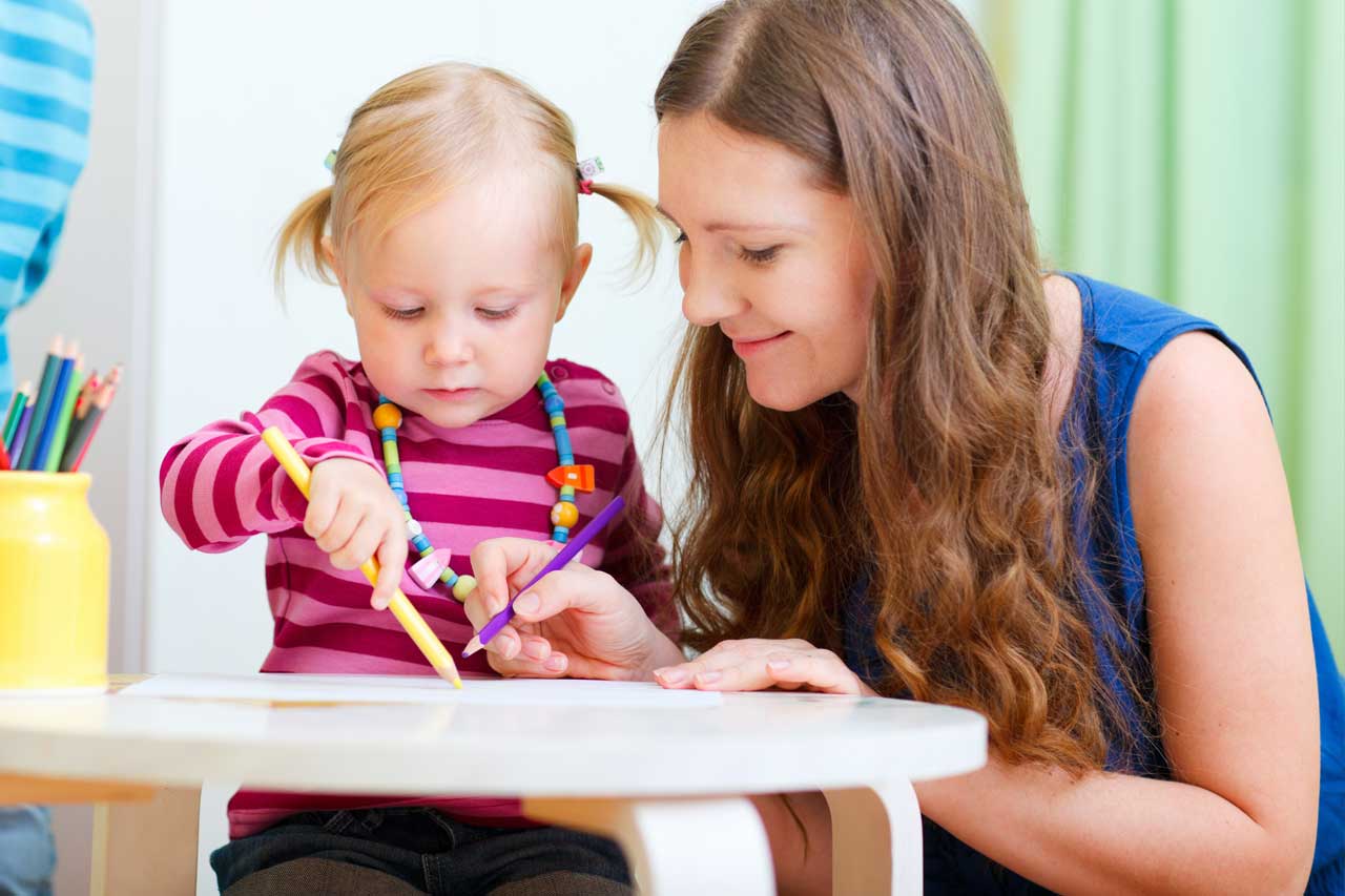 eine Erzieherin malt zusammen mit einem kleinen Mädchen.